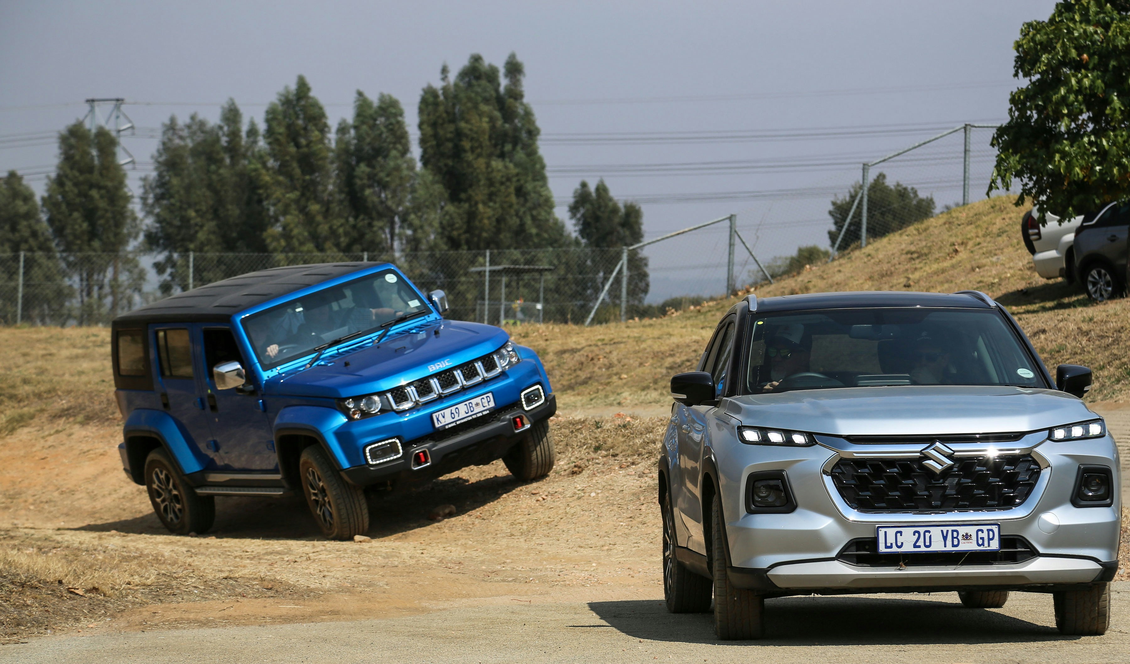 two cars driving on a dirt road next to a hill