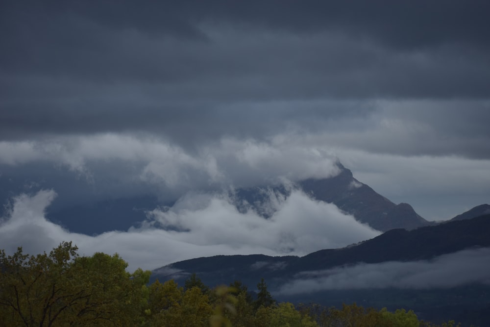 a mountain covered in clouds and trees under a cloudy sky