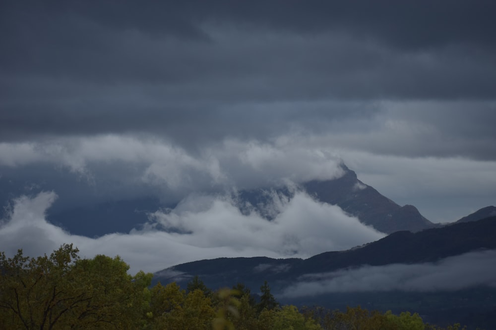 una montagna coperta di nuvole e alberi sotto un cielo nuvoloso