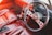A vintage car interior featuring a red leather upholstery. The dashboard includes a classic analog speedometer and other gauges. A black steering wheel with metal accents and a gear shift is prominently visible. The overall design gives a retro automotive vibe.