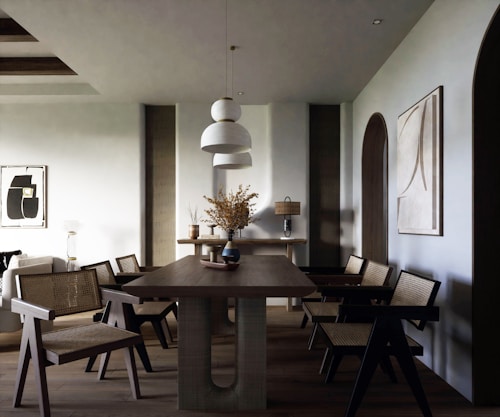 A modern dining room with a minimalist aesthetic featuring a wooden dining table and wicker chairs. Two large abstract paintings adorn the walls, and a trio of pendant lights hang overhead. A vase with dried branches sits on the table, complemented by soft lighting and neutral tones.