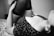 A monochrome image depicts a person lying on a patterned surface. The focus is on the upper body, revealing a floral patterned top and sheer stockings. The scene appears intimate and artistic, with a soft and blurred background.