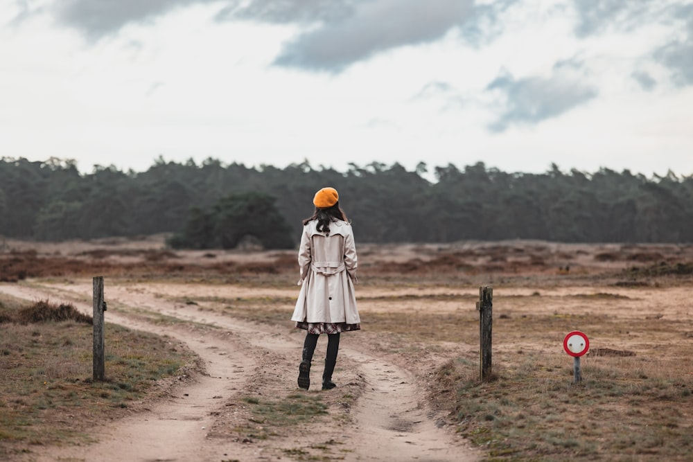 a woman standing on a dirt road in a field