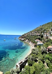 A vibrant coastal landscape with turquoise sea, golden sandy beach, and locals enjoying a sunny day.