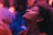 A person with a serene expression is captured in close-up, eyes closed, and head slightly tilted back. The background is softly blurred, creating a sense of focus and intimacy. The scene is bathed in warm, ambient lighting with shades of purple and orange.