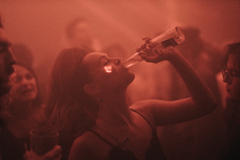 a woman drinking from a bottle while standing in front of a group of people