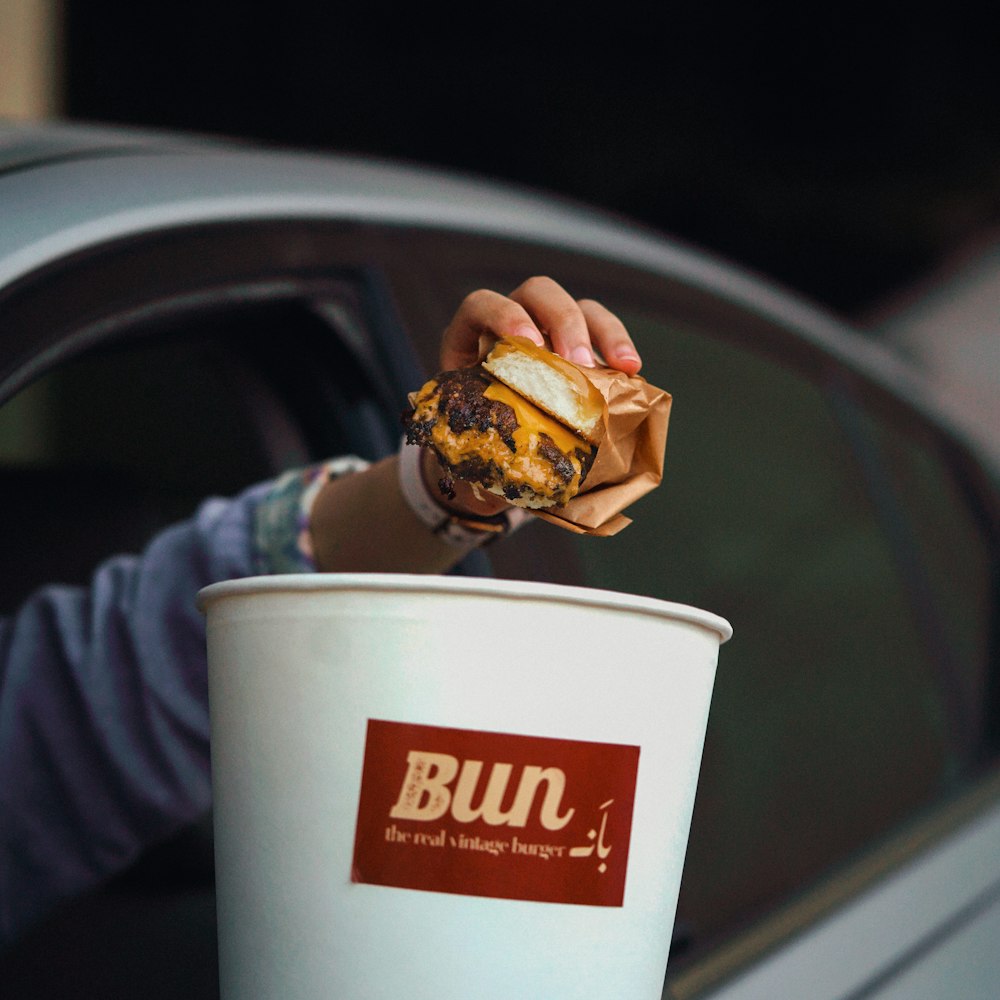 a person holding a doughnut in a paper cup