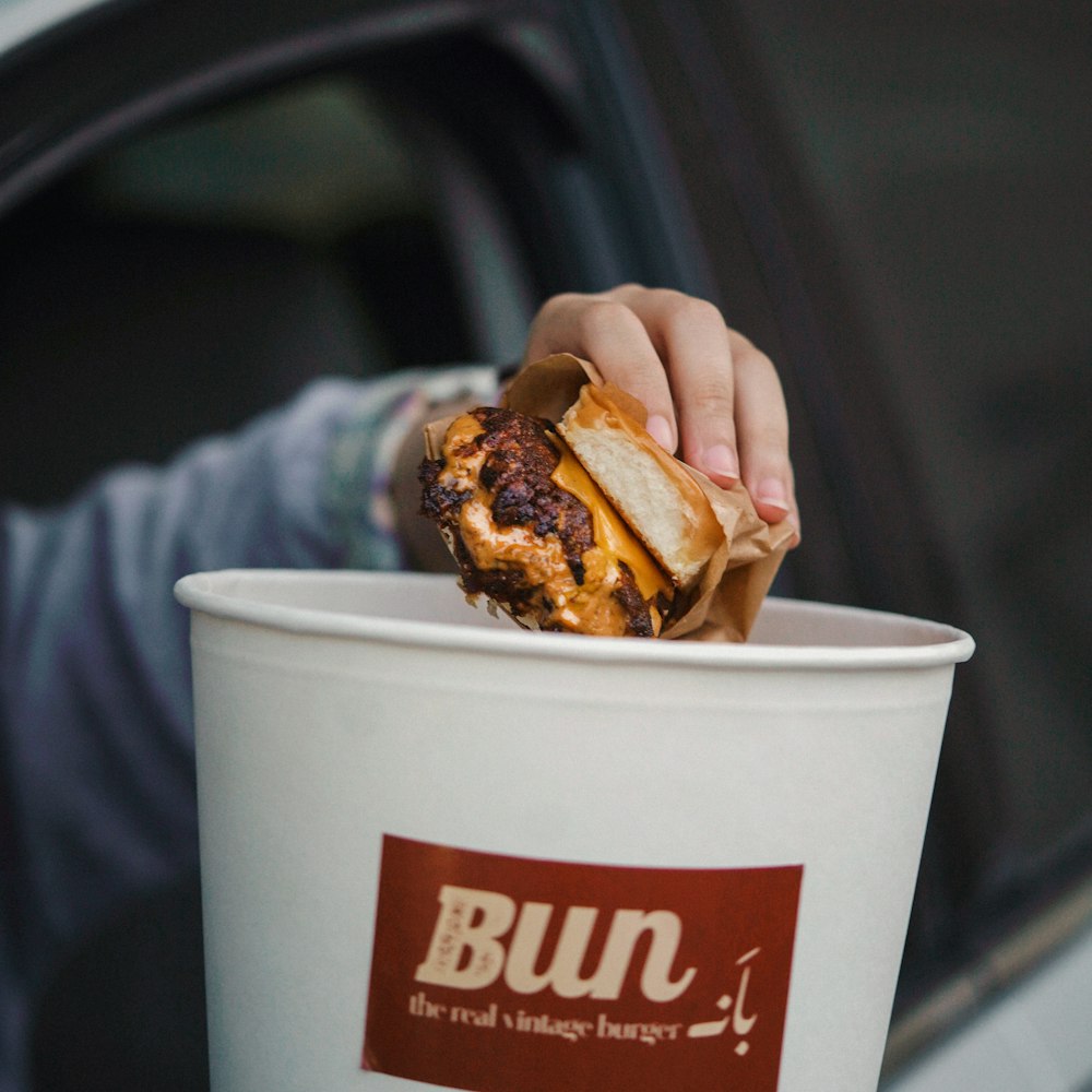 a person holding a hamburger in a paper cup