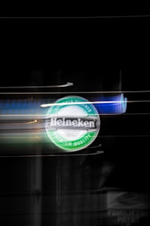 A blurred image featuring a Heineken logo in the center, illuminated against a dark background. The motion blur suggests movement, with visible light streaks.