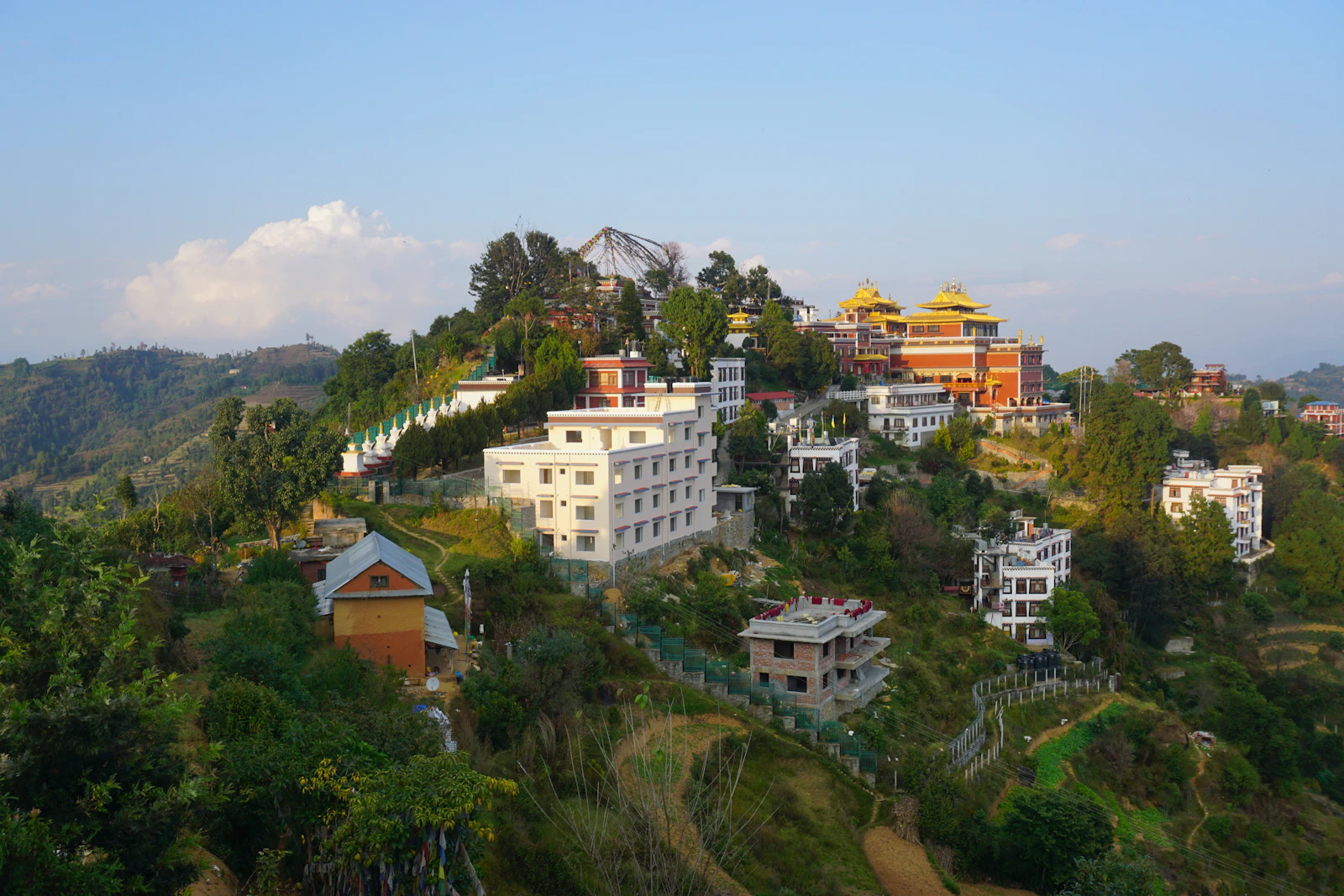 The gilded roofs of Thrangu Tashi Yangtse monastery on the hilltop at Namo Buddha, above wooded slopes and village houses