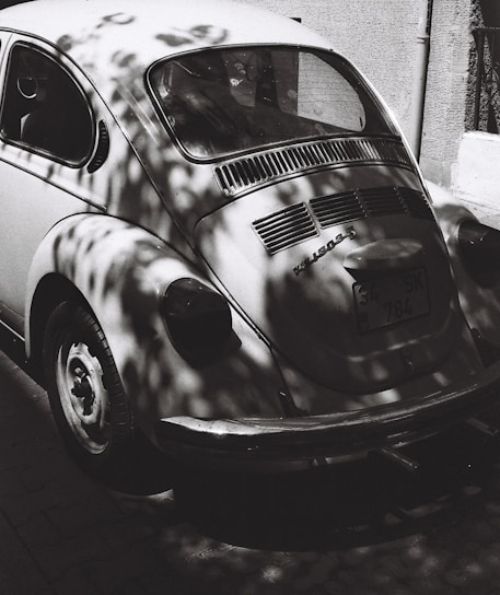 A sleek, minimalist photo of a vintage Volkswagen Beetle parked on a sunlit street.