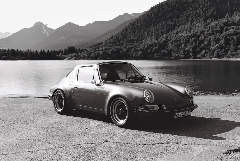 a black and white photo of a car parked by a lake