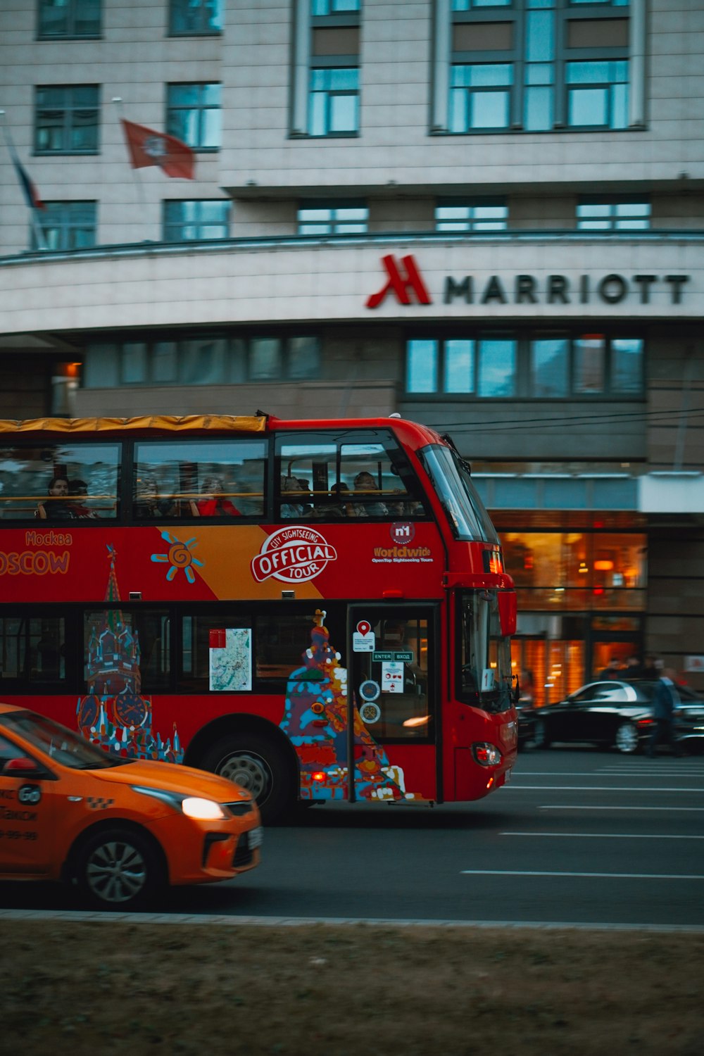 a red double decker bus driving past a tall building