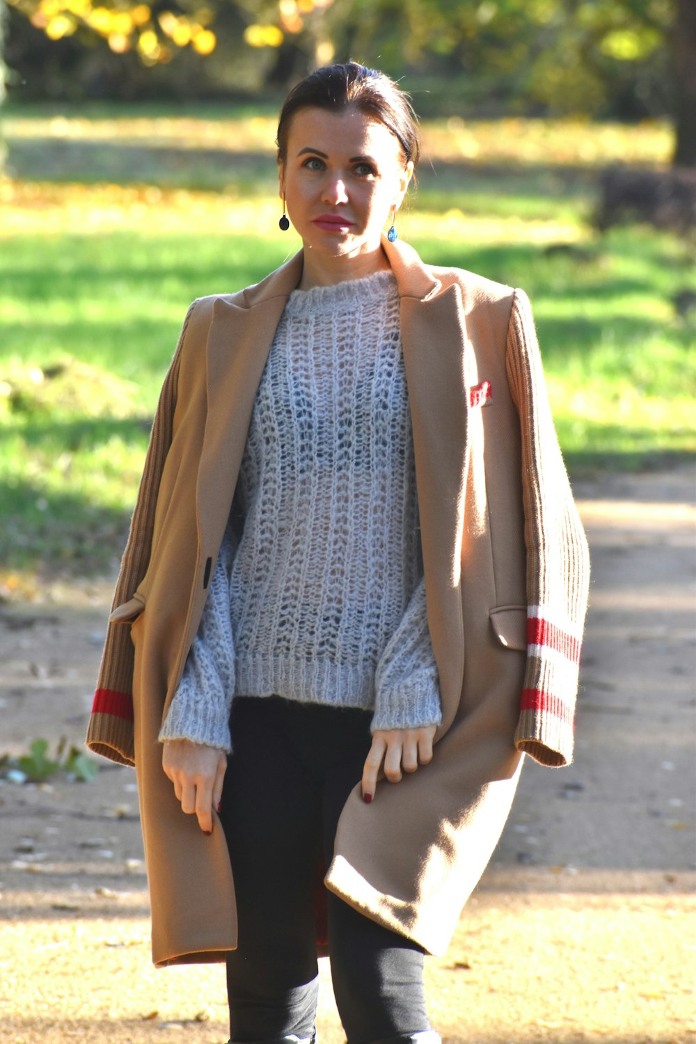 a woman walking down a dirt road wearing a coat