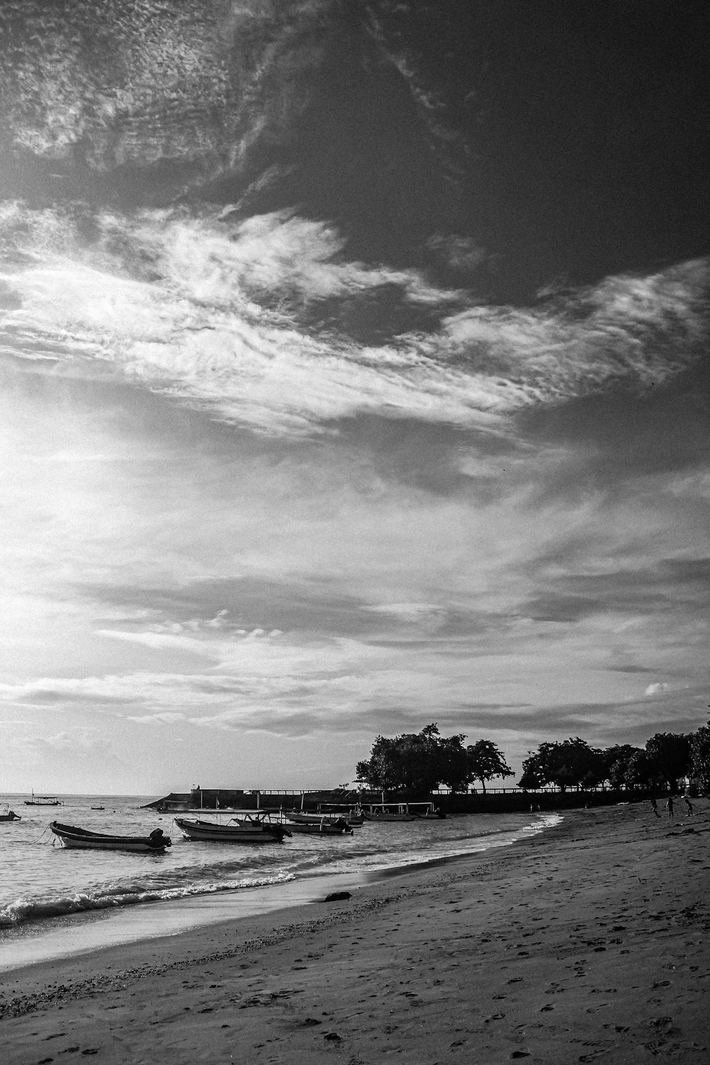 a black and white photo of a beach with boats