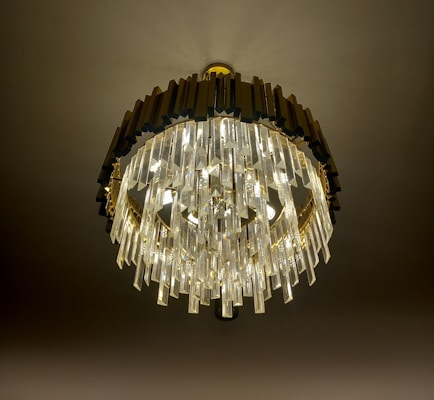 A luxurious chandelier with multiple layers of crystal prisms hangs elegantly from the ceiling. The dark frame contrasts with the bright, sparkling crystals that catch and reflect light beautifully.