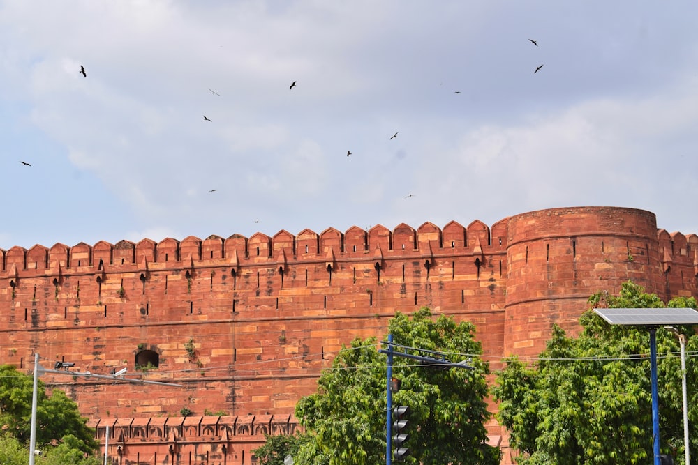 birds flying over a large brick building near trees