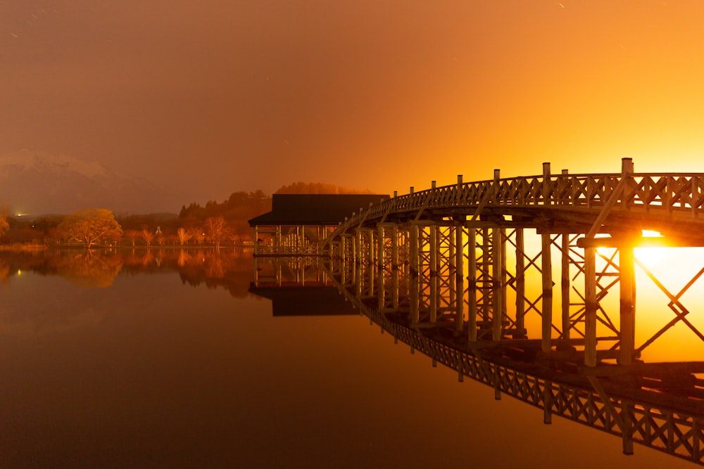 the sun is setting on a bridge over a lake