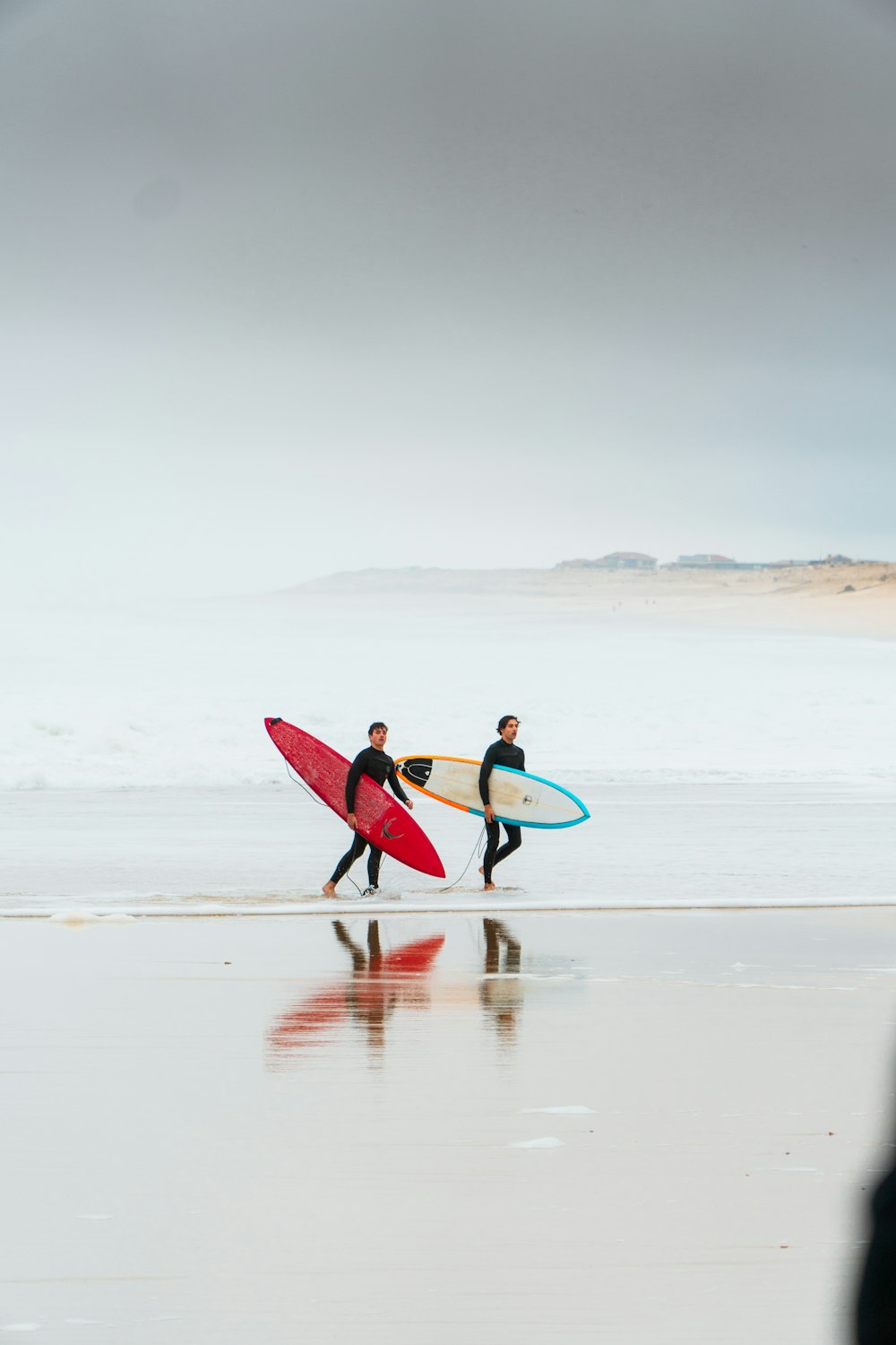 two surfers walking on the beach with their surfboards