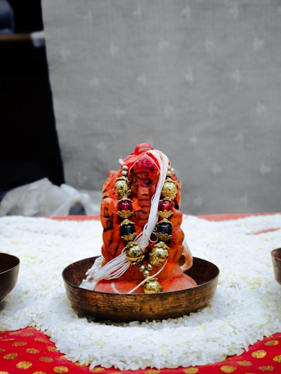 A close-up of a silver miniature human mould used in traditional pooja offerings, resting on a brass plate.