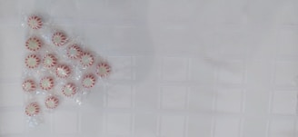 A group of peppermint candies arranged in a triangular pattern on a textured white surface. The candies are individually wrapped and have a red and white striped pattern.