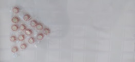 A group of peppermint candies arranged in a triangular pattern on a textured white surface. The candies are individually wrapped and have a red and white striped pattern.