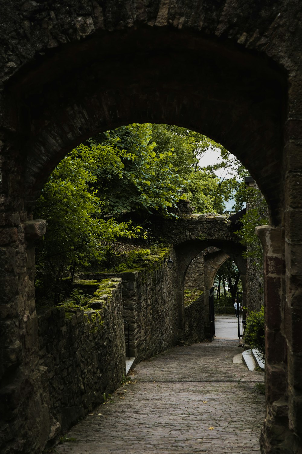 a stone walkway with an arch leading into a park