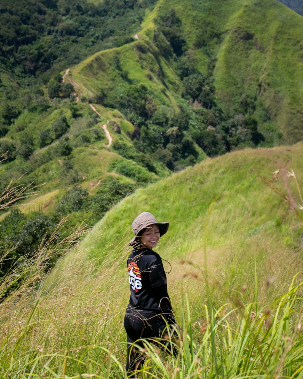 a woman in a hat standing on a lush green hillside