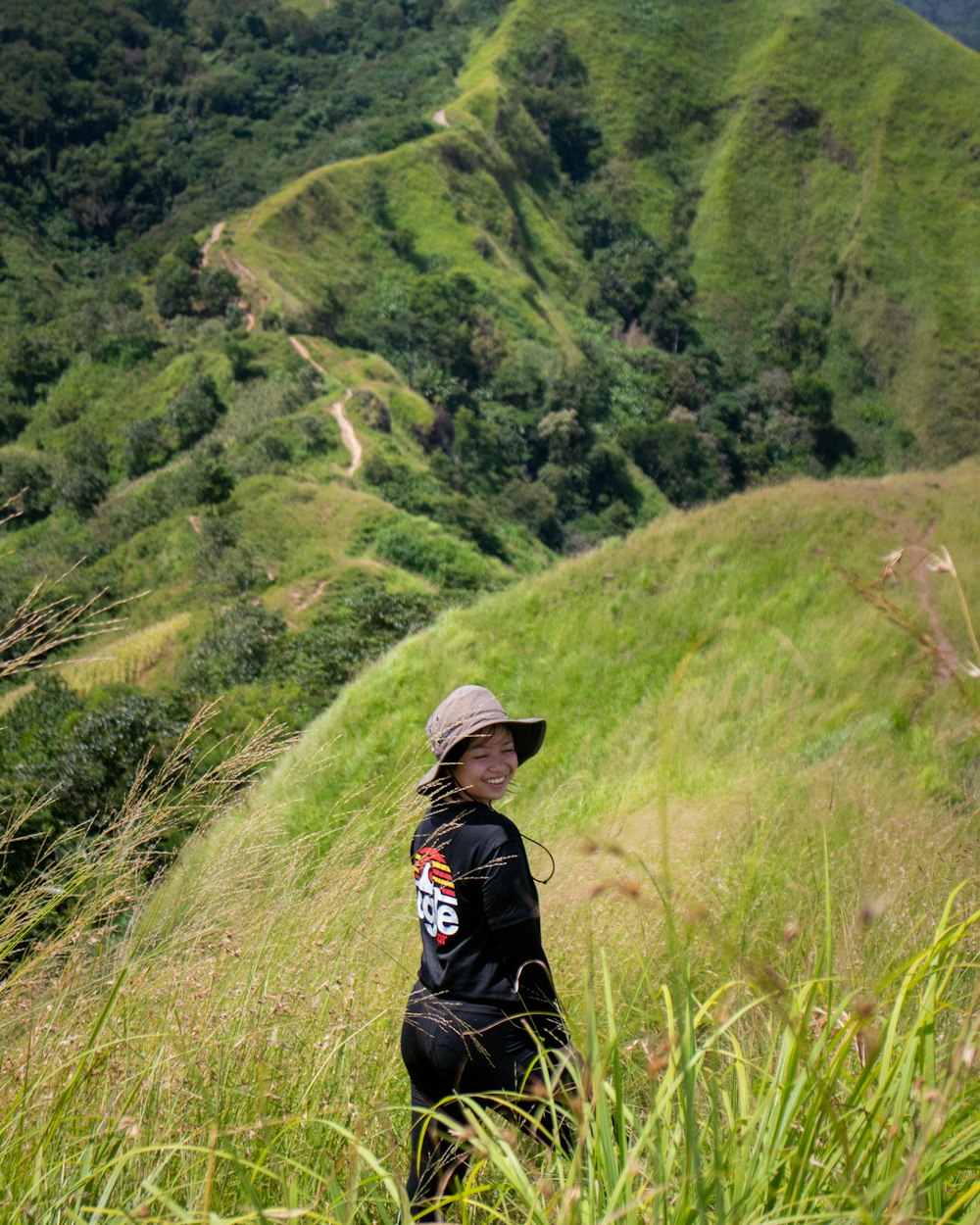 une femme coiffée d’un chapeau debout sur une colline verdoyante