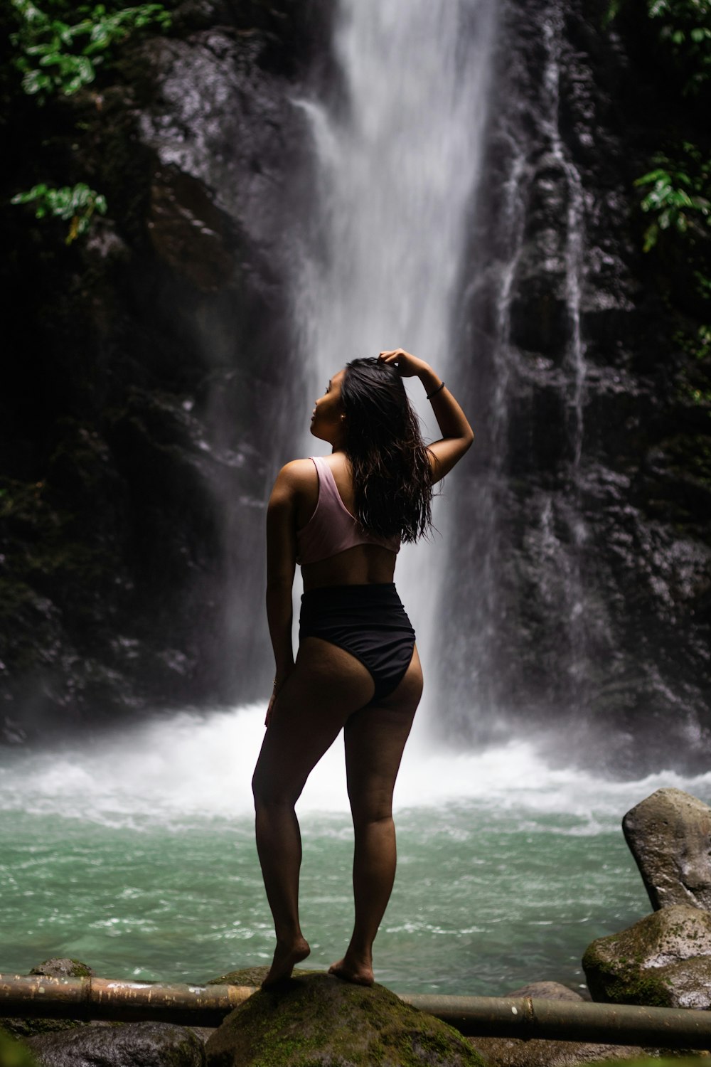 a woman in a bathing suit standing in front of a waterfall