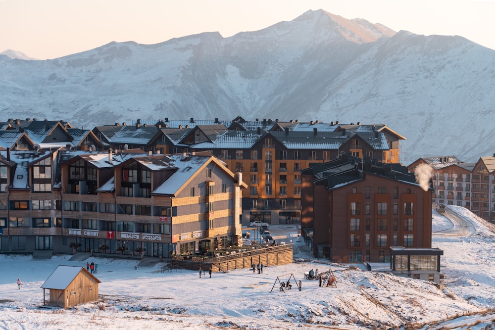 a group of buildings in the snow with mountains in the background