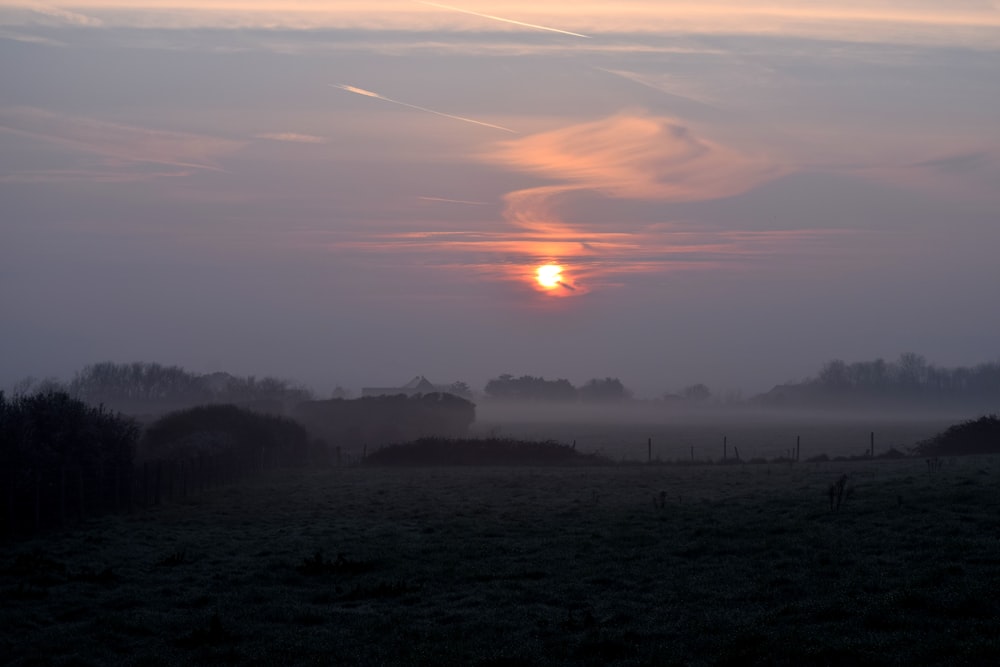 the sun is setting over a foggy field