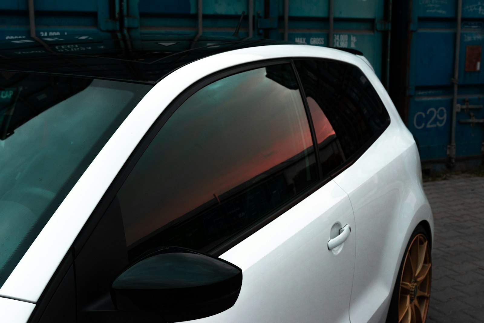 Dark tinted rear side window on a blue car reflecting trees and streetlights