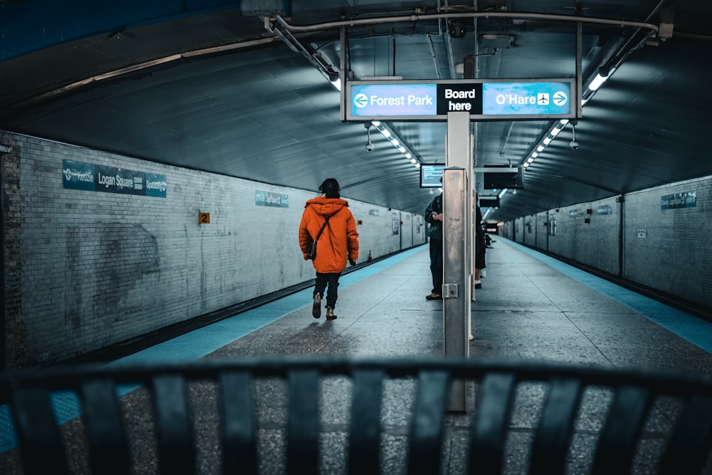 a person in an orange jacket walking down a subway platform