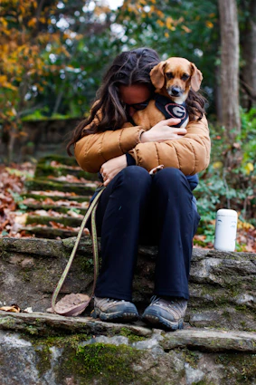 a woman sitting on a rock holding a dog
