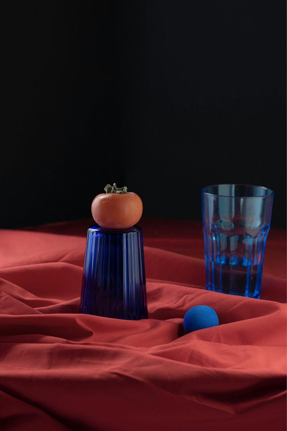 a blue glass and a tomato on a red cloth