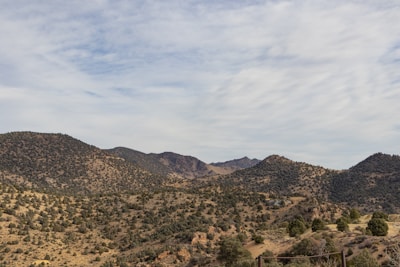 Rolling hills covered with scattered trees under a partly cloudy sky. The landscape appears dry with various shades of green and brown, indicating a semi-arid environment.