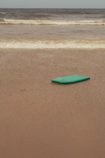 A sturdy beginner surfboard resting on a sandy beach with gentle waves in the background