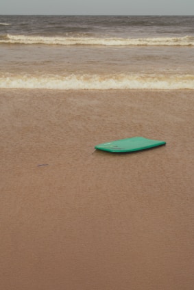 A colorful beginner softboard resting on a sandy beach with gentle waves in the background.