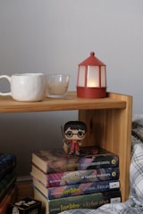 A cozy writing nook with a stack of colorful children’s books and a dragon figurine beside a glowing lamp.