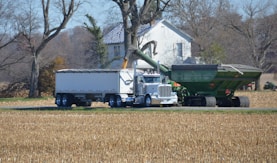 a tractor trailer hauling a trailer with a house in the background