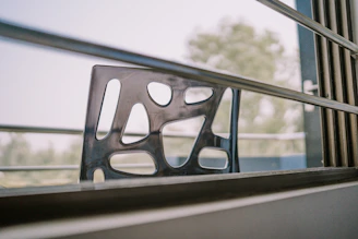 Aluminum lounge chair with clean lines set beside a large window with greenery outside.