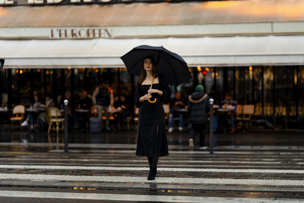 a woman walking across a street holding an umbrella