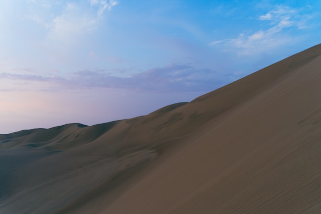 A serene early morning landscape with soft sand dunes under a pastel sky, evoking calm and openness.