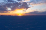 Sunset casting warm reddish hues over the vast Uyuni salt flats with travelers admiring the view