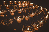 Rows of elegant metal candle holders lined up on a rustic wooden table, catching the light.