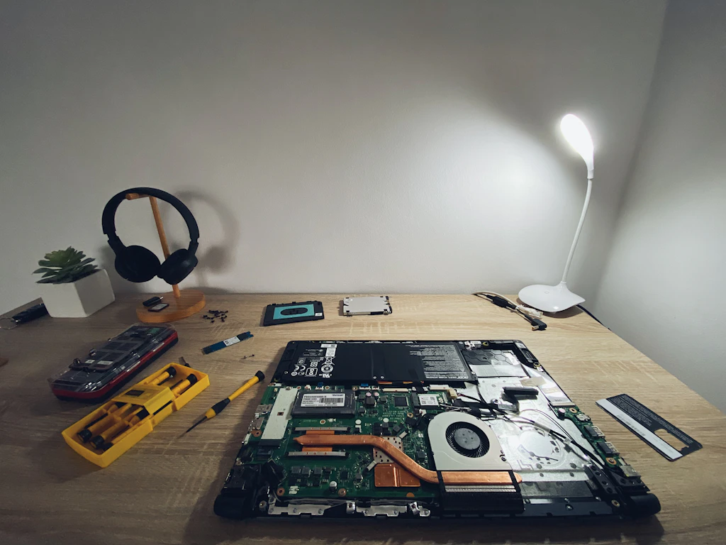 An open laptop on a workbench with screwdrivers and a desk lamp