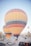 Multiple large hot air balloons are prepared for flight in a desert-like landscape with rocky formations. Several vehicles, including cars and jeeps, are parked around the area, with people gathered near the balloons. The scene conveys a sense of adventure and exploration.
