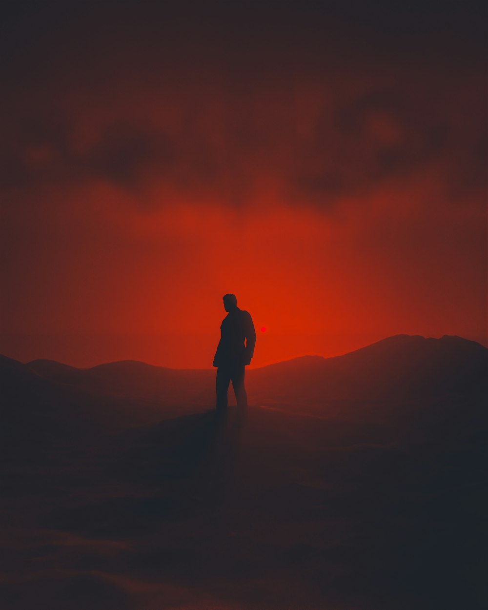 a man standing on top of a hill under a red sky