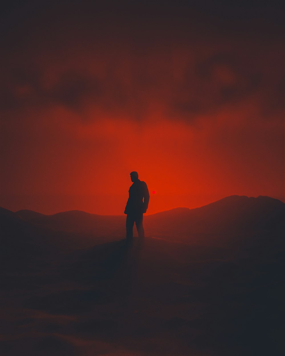 un hombre de pie en la cima de una colina bajo un cielo rojo